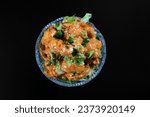 Dynamite shrimp in a glass cup with scallion sprinkles on top on a black table starter seafood