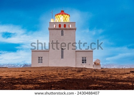 Dyrholaey lighthouse on icelandic peninsula with tall guidance building near ocean shoreline. Majestic colorful tower beacon of light used for navigation and visibility in iceland.