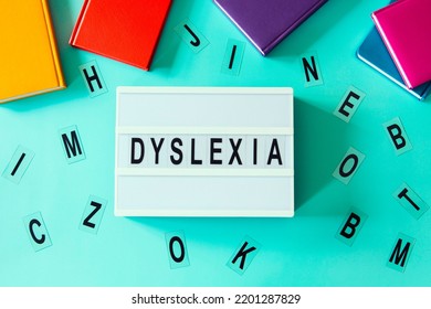 Dyslexia Awareness, Help Children With Reading, Learning Difficulties Concept. Lightbox With DYSLEXIA Word. Colorful Books And Different Letters On Light Blue Background. Top View