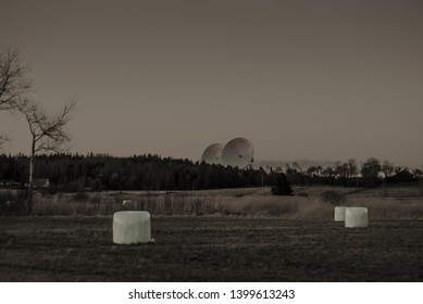 Dystopian View Of Large Satelite Dishes Behind A Forest And Fields.