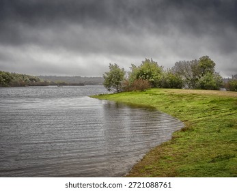 Póvoa e Meadas Dam forms the second largest reservoir in the district of Portalegre (only surpassed in size by the Caia Dam) and is located in the parish of Póvoa e Meadas, municipality of Castelo de Vide, about 5 km northwest of this town.The hydroelectric power plant consists of a Francis group with a total installed power of 0.74 MW. The average energy produced per year is 1.6 GWh. Source: WikipediaCastelo de Vide, Portugal. Storm clouds gathering over a peaceful lake with green grass along the shore