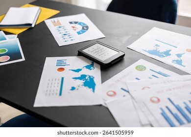 E reader displaying placeholder text sits on a desk amongst various business papers featuring charts, graphs, and a world map, suggesting data analysis and global business strategy