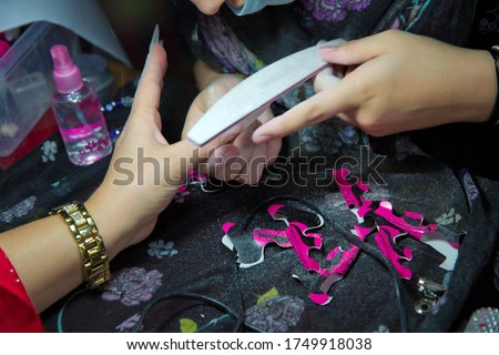 Each of the nails is filed before the artwork is painted onto the nail. Rough up the top of the nail for better adhesion. Manicure in beauty salon. Selective focus on nail polish removing pen.