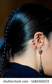  Ear Cartilage Piercing. Helix Piercing. A Puncture In The Curl Of The Ear Or In The Upper Part Of The Ear. The Pierced Ear Of A Girl With Long Black Hair And A Braided Pigtail.