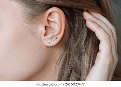 Ear piercing. Cropped shot of a young woman wearing three stud earrings on the earlobe. Jewelry with gemstones, accessories, a cross with fianits