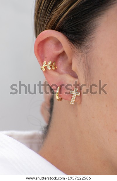 In ear\
are three earrings. One is a small cross with zircons, the second\
is a hoop and the last is a gold ear\
cuff.