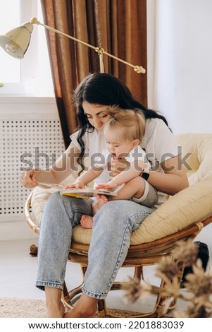 Early childhood development. Mom is reading a book to her baby while sitting in a chair.