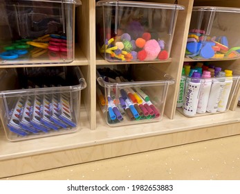 Early Childhood Education Preschool Classroom. Wooden Shelves With Art Supplies In Clear Bins - Scissors, Paints, Markers, Pipe Cleaners And Shapes. No People. 