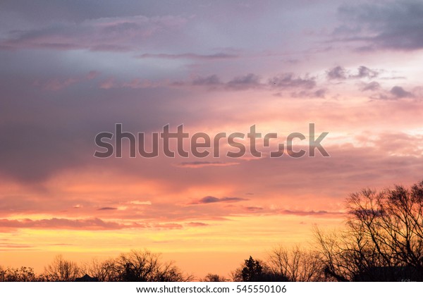 An early\
dawn winter\'s scene of the different colored, colorful cloud\
formations, with trees dividing earth from\
sky
