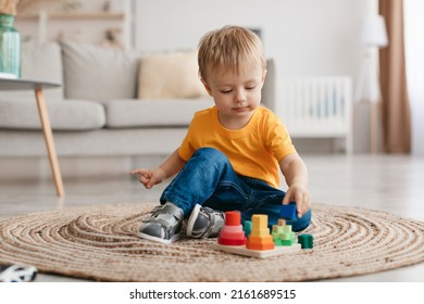 Early development concept. Little toddler boy playing with educational wooden toy at home, sitting in living room interior, free space. Child with wooden colorful stacking and sorting toy - Powered by Shutterstock