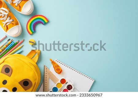 Early education essentials. Top-down view of a lively kid's school bag filled with colorful school supplies and yellow sneakers on a pastel blue surface, copy-space ideal for text or promotional use