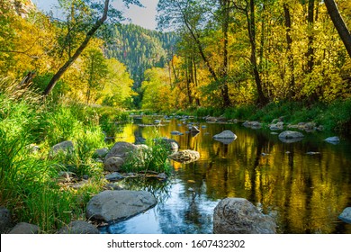 Early fall colors over Oak Creek outside Sedona, Arizona with water flowing over and around rocks.