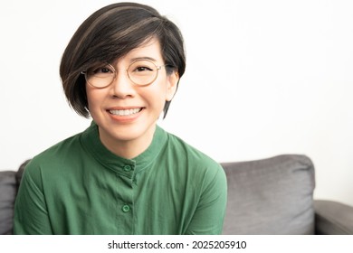 Early To Mid-40s Presbyopia Eyesight. Portrait Of Stylish Asian Middle-aged Woman In Green Outfit And Round Eyes Glasses Smiling With Satisfaction. Eyewear, Ageing, Progressive Lenses, Optic Concept.