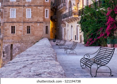 The early moning on the waterfront of Senglea city (or Civitas Invicta).  The view of the Triq is-Sirena street with the openwork forged metal benches in the sunrise light. Malta