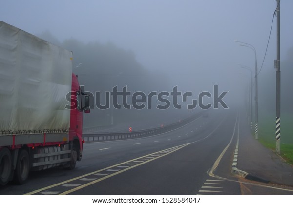 Early morning driving truck on highway in fog.\
Autumn, dry weather, foggy grey sky. One truck on the road. Lonely\
vehicle on the motorway.
