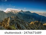 Early morning in High Tatras mountains, Slovakia. An amazing view of high rocky peaks surrounded by clouds during golden hour. Sunrise over High Tatras mountains from the top of Koprovsky peak.