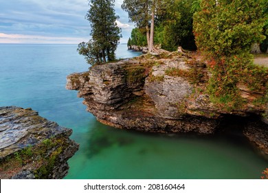 Early morning long exposure photo at Door County, Wisconsin's Cave Point, on Lake Michigan, reveals rocky cliffs, colorful waters, and a cloudy sky.