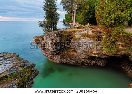 Early morning long exposure photo at Door County, Wisconsin's Cave Point, on Lake Michigan, reveals rocky cliffs, colorful waters, and a cloudy sky.