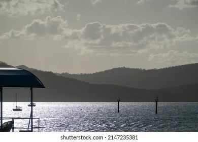 Early Morning Mist On The Mountains And Sunlight On The Water Offshore From A Tourist Resort.  Opaque Cloudy Sky Landscape.