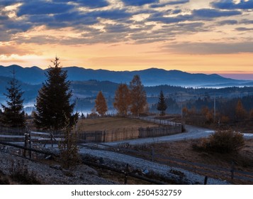 Early morning misty autumn slopes of Carpathian Mountains and rural road in mountain village (Yablunytsia village and pass, Ivano-Frankivsk oblast, Ukraine). Goverla and Petros mountains in far. - Powered by Shutterstock