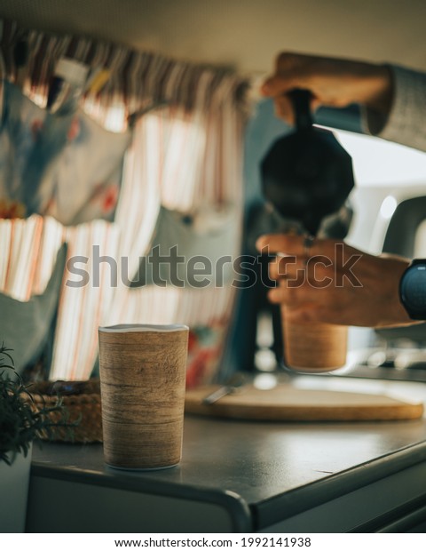 Early morning person\
serving coffee on the background from an Italian coffee pot to a\
cup in a van in vintage coffee color tone while another cup waits\
to be served