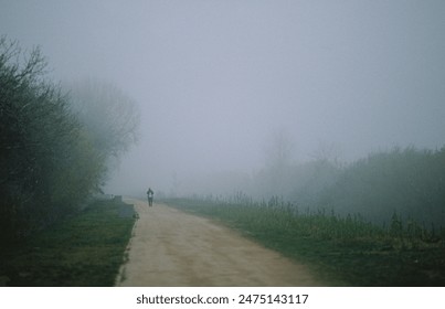 Early morning shot on film of a solitary figure walking down a foggy rural road flanked by trees and bushes - Powered by Shutterstock