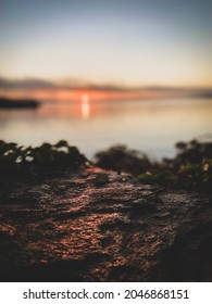 Early Morning Sun Reflecting Off Lake And Shining On Flat Rock On Coastline. Selective Focus On The Rough Surface Of Stone.