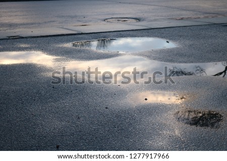 Early morning sunrise sky reflected in a puddle of water on pavement 