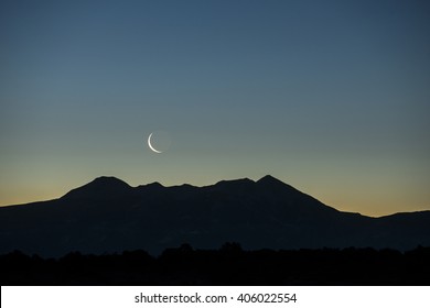 Early morning waning waxing crescent moon rising over graphic silhouetted mountain