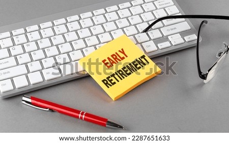 EARLY RETIREMENT text on a sticky with keyboard, pen glasses on a grey background