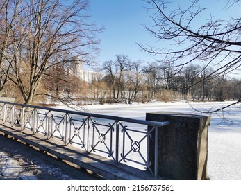 Early spring in the city park.  Metal railings of the bridge, snow on the lake, trees without leaves against the blue sky. - Powered by Shutterstock