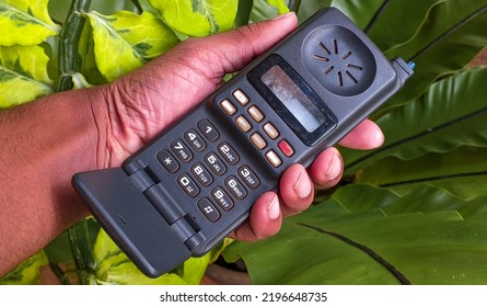 Early Stages Old Vintage Mobile Phone, Cellular Phone, Cell Phone, Cellphone, Handphone Or Pocket Portable Telephone In Hand On Green Background