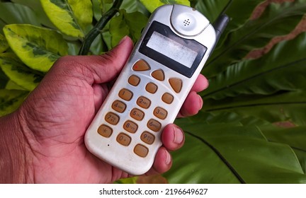 Early Stages Old Vintage Mobile Phone, Cellular Phone, Cell Phone, Cellphone, Handphone Or Pocket Portable Telephone In Hand On Green Background