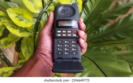 Early Stages Old Vintage Mobile Phone, Cellular Phone, Cell Phone, Cellphone, Handphone Or Pocket Portable Telephone In Hand On Green Background