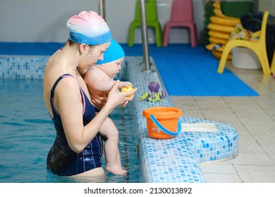 Early swimming coach training to swim baby boy in indoor pool. Playing activity for infant with mother, child physical development in water with joy and fun. Accessories and toys for diving lesson - Powered by Shutterstock