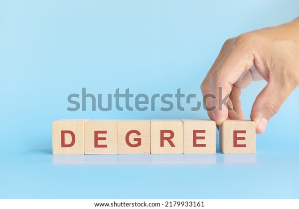 Earn a college degree concept. Human hand\
completing the word degree on wooden\
blocks.