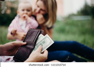 Earning Money For Family. Male Hand With Wallet And US Dollar Bills At Family Blurred Background. Financial Support, Business, Family, Alimony, Maintenance, Investing In Children Concept