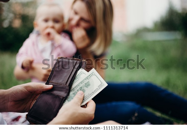 Earning money for family. Male hand with wallet\
and US dollar bills at family blurred background. Financial\
support, business, family, alimony, maintenance, investing in\
children concept