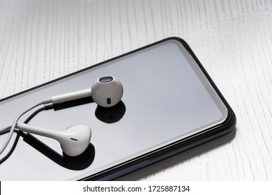 Earphones Over A Mobile Smart Cell Phone Device Reflective Screen Minimalist Image Depicting A Podcast Or Music Listener Concept 