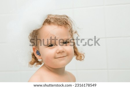 Earplugs for children, earplugs for swimming. A little girl is sitting in a bath with earplugs. Ear diseases in children. Protection against water ingress into the ears.