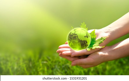 Earth crystal glass globe ball and maple leaf in human hand on grass background. Saving environment, save clean green planet, ecology concept. Card for World Earth Day.