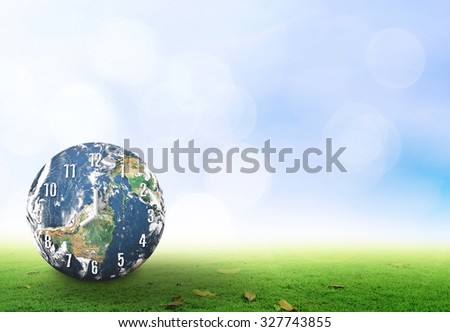 Earth day concept: Clock of planet over green grass and blue sky background. Elements of this image furnished by NASA