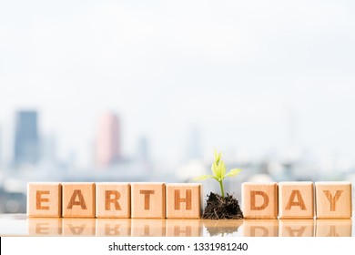 Earth Day, ein Tag der Erziehung über Umweltfragen Konzept. Holz versperrt Wort mit wachsenden Pflanzen- und Stadtsonnenhintergründen.