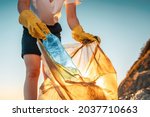 Earth day. A female activist puts a plastic bottle in a garbage bag. Close-up. The concept of environmental conservation and coastal zone cleaning.