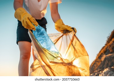 Earth day. A female activist puts a plastic bottle in a garbage bag. Close-up. The concept of environmental conservation and coastal zone cleaning. - Shutterstock ID 2037710663