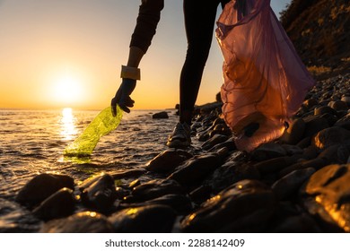 Earth day. A volunteer take a plastic bottle by the sea or river holding a plastic trash bag. Concept of coastal cleanup. - Powered by Shutterstock