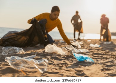 Earth day. Volunteers activists collects garbage cleaning of beach coastal zone. Woman mans with trash in garbage bag on ocean shore. Environmental conservation coastal zone cleaning. Blurred image - Powered by Shutterstock