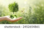 Earth Day or World Environment Day, environmentally friendly concept. Tree growing on globe and yellow butterfly in hand on green background. Save planet and protect nature, sustainable lifestyle.