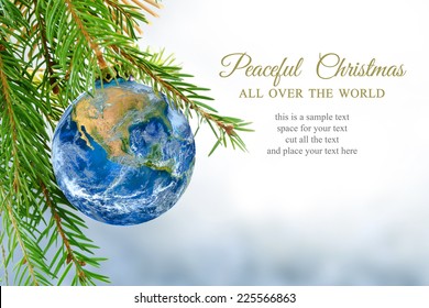 earth globe as Christmas ball hanging in fir branch, message: peaceful Christmas all over the world, symbol, metaphor, copy space, bright snowy background. Elements of this image furnished by NASA.