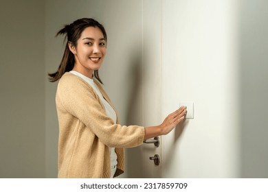 Earth Hour. Asian beautiful woman turn off or on the light to saving electrical energy. Finger pushing light switch turn on or off. White switch - Shutterstock ID 2317859709